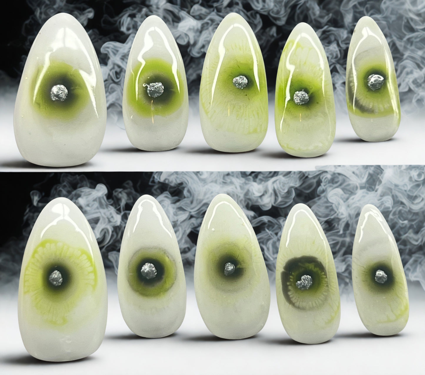 Astral Eye press-on nails featuring a glossy white base with a green iris bloomed in the center of each nail. A hand-painted metallic silver dot sits in the middle of the iris as the pupil. Medium stiletto shape shown against a smoky, atmospheric background.