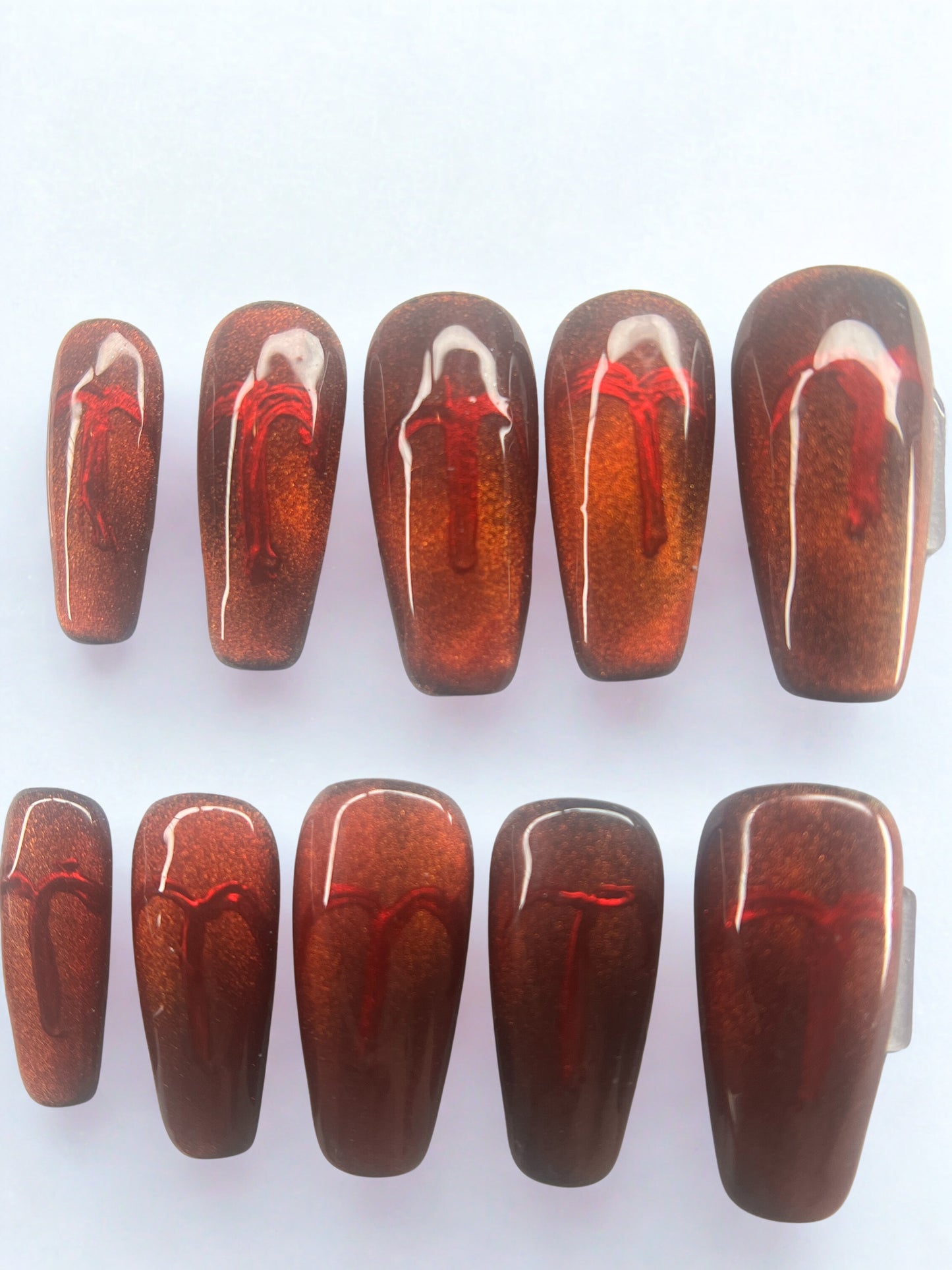 Square shaped press on nails with a black base and a shifting red-to-gold magnetic velvet cat eye finish.