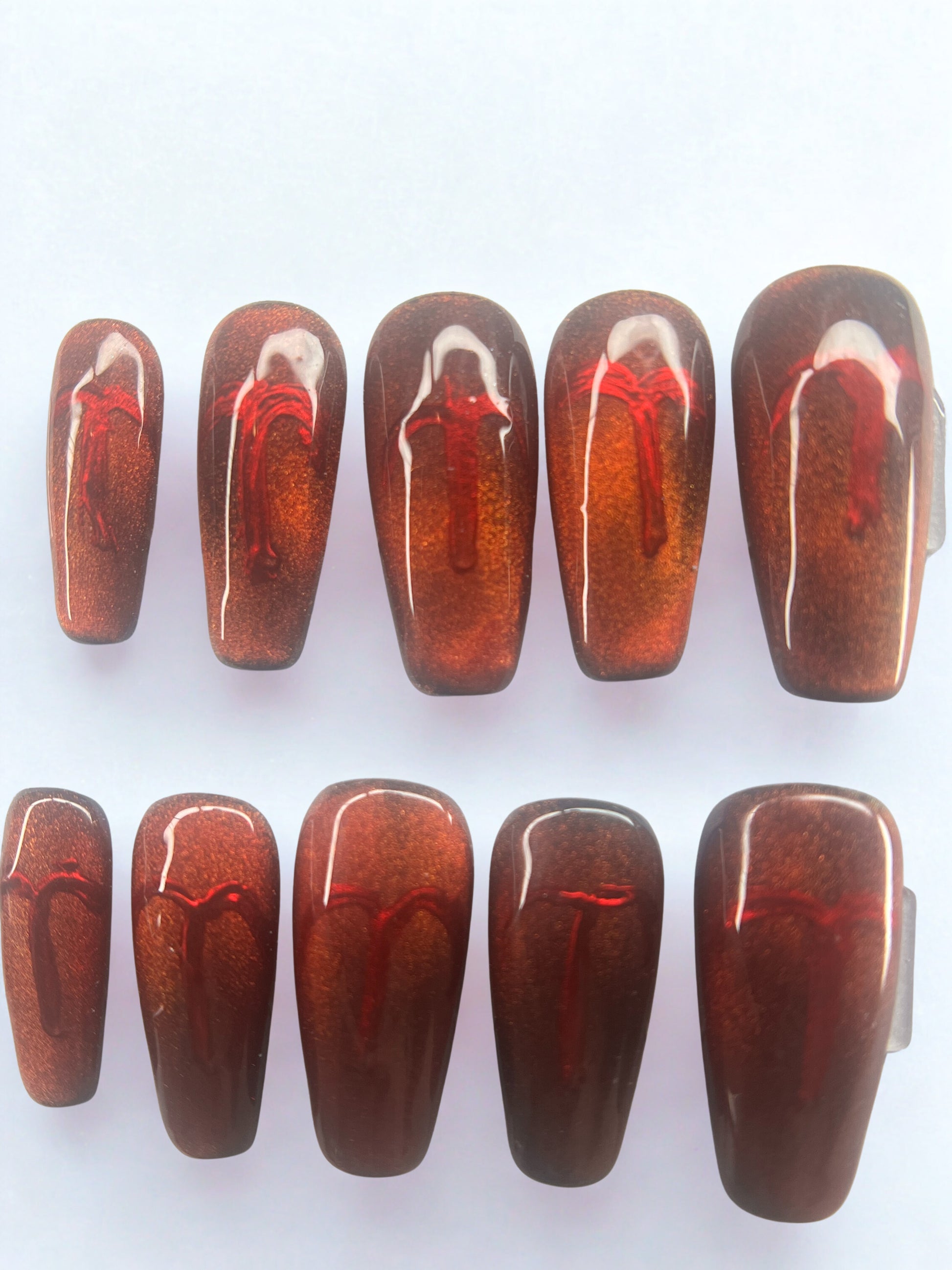 Square shaped press on nails with a black base and a shifting red-to-gold magnetic velvet cat eye finish.