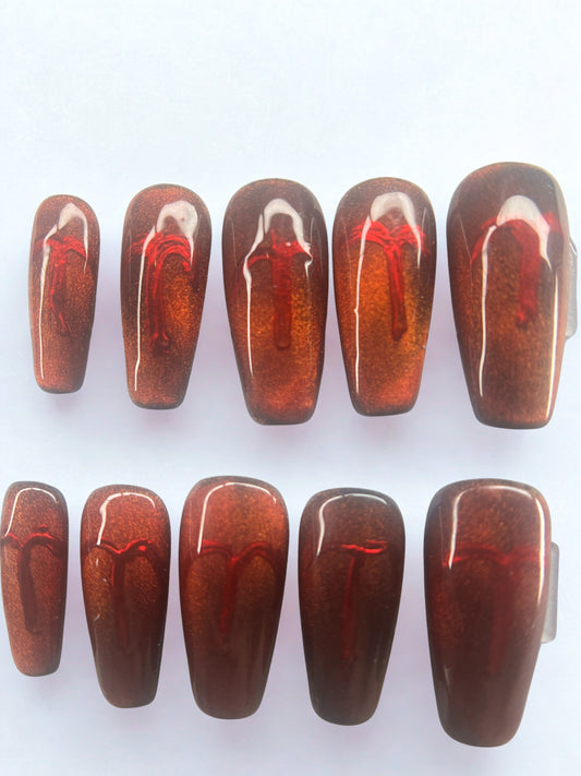 Square shaped press on nails with a black base and a shifting red-to-gold magnetic velvet cat eye finish.