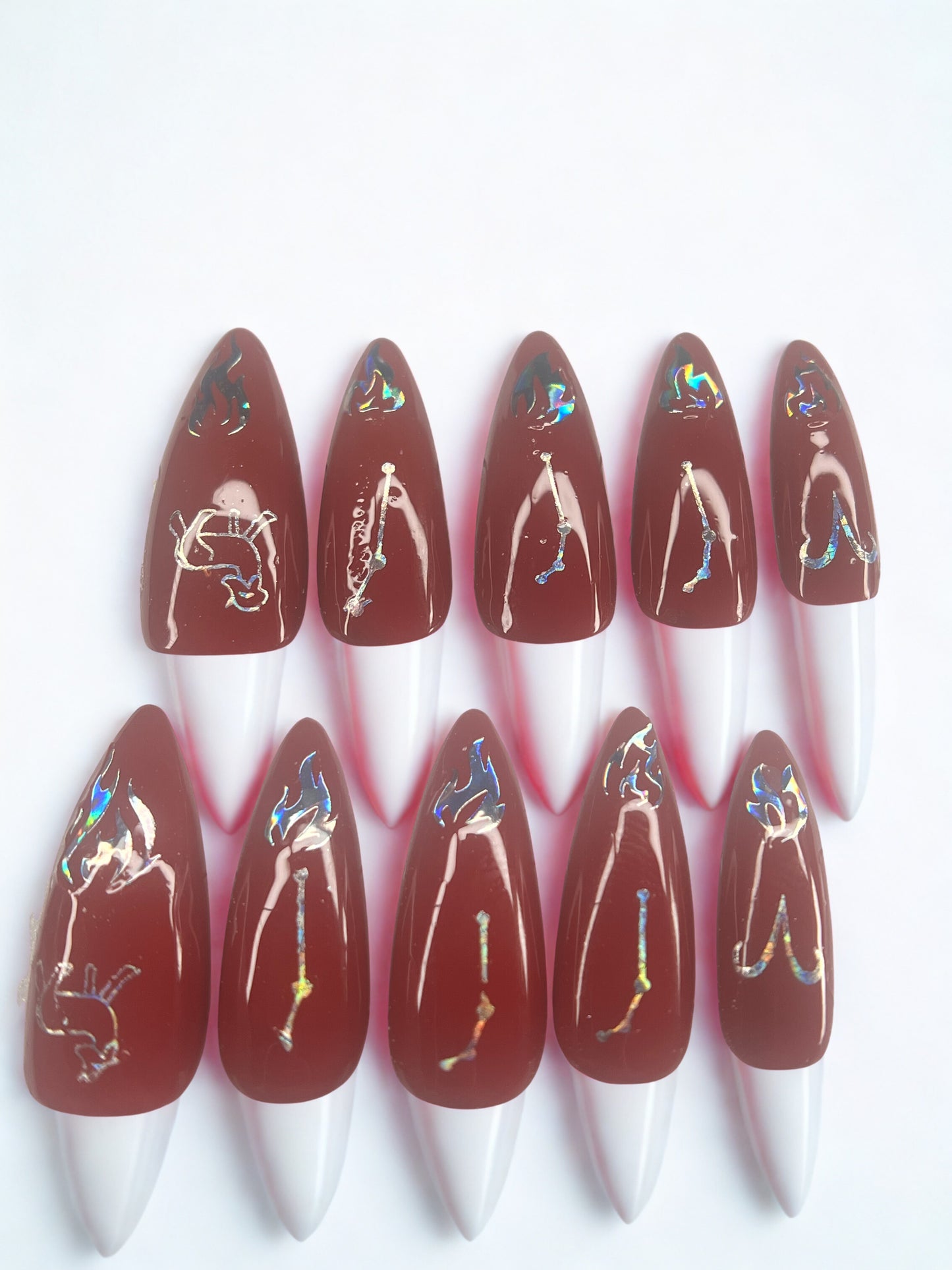 Medium stiletto press on nails in a deep crimson red featuring various holographic Aries zodiac stickers and constellations.