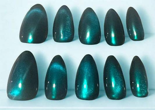 Celestial Emerald press-on nails with a triple-layered finish. A base of iridescent mermaid chrome is topped with a magnetic glass cat-eye and finished with a translucent turquoise jelly. The result is a deep, glowing teal with a velvet-shimmer effect on an almond shape.