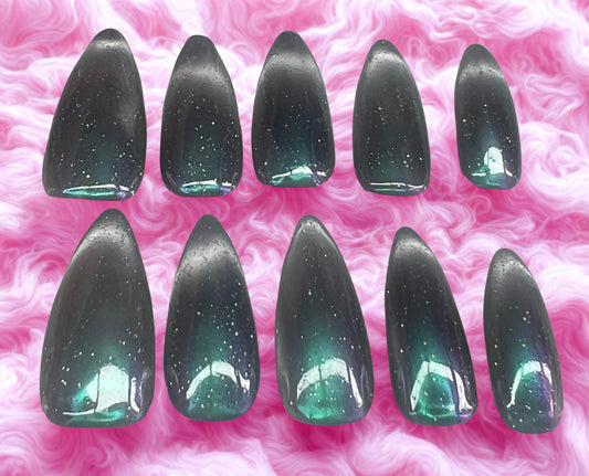 Galactic Glimpse press-on nails featuring a milky white base with a purple and green gradient chrome. Includes a magnetic glass cat-eye shimmer on the tips (smile lines) and a multi-colored holographic glitter topcoat. Medium stiletto shape against a pink fur background.