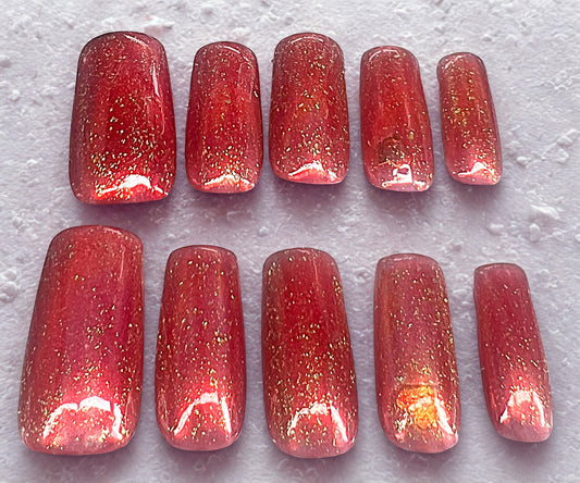 Golden Love press-on nails featuring a red jelly finish over a pink base. Includes gold foil glitter flecks and hidden heart stickers encapsulated under the jelly on the ring fingers. Medium square shape with a high-gloss, translucent depth.