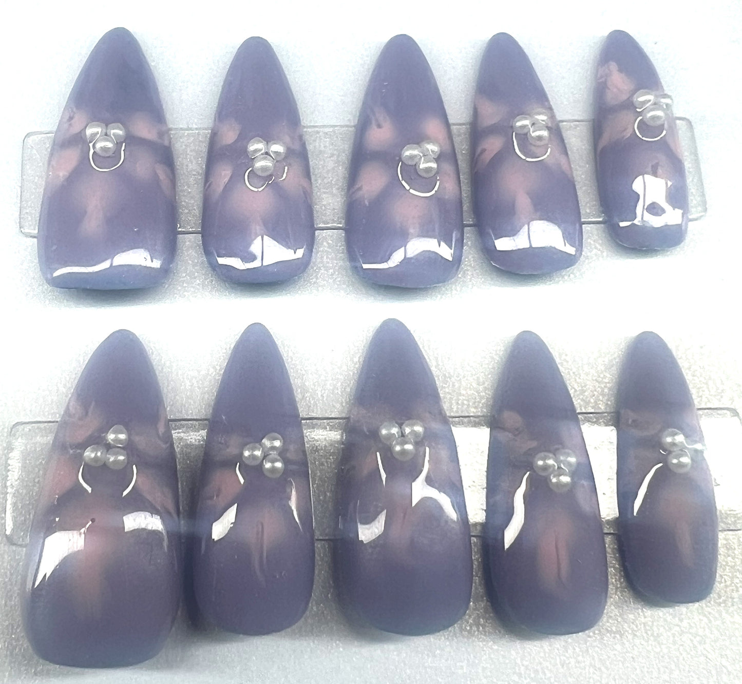 Handmade press on nails with a solid lavender purple base. Each nail features soft pink blooming flower art in the center, accented with three tiny white pearls. The nails are shown in a long pointed almond shape with a glossy topcoat.