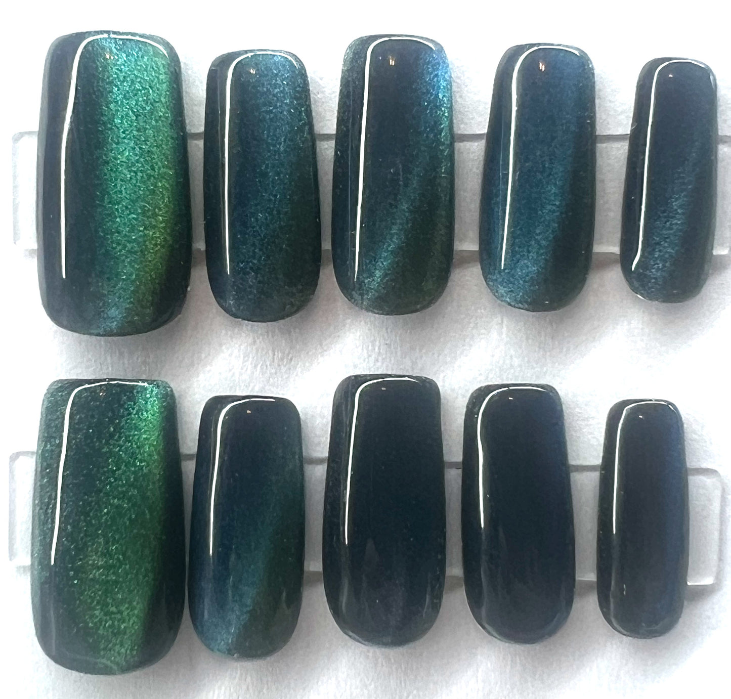 A professional close-up photo of ten handmade press-on nails with a high-gloss obsidian black base. Each nail features sharp, dimensional green and blue diagonal chatoyant cat-eye magnetic lines.