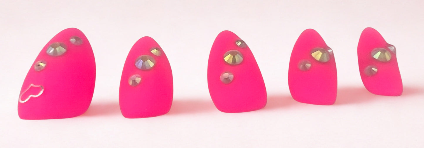 Electric Matte press-on nails in vibrant neon pink with a velvet matte finish. Features a silver heart charm on the thumb and three sparkling rhinestones on each nail. Medium almond shape shown against a clean white background.