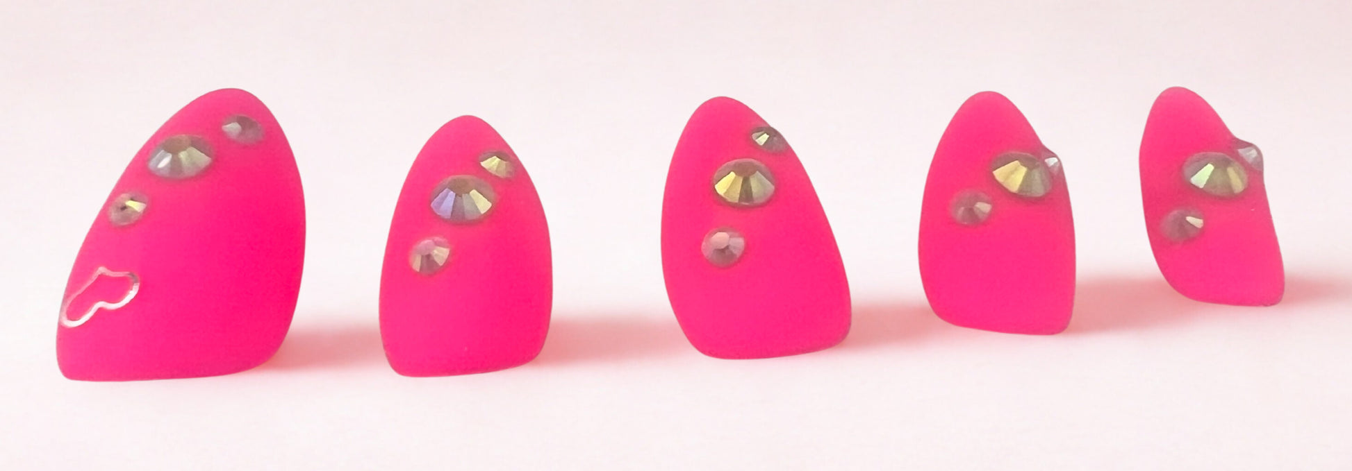 Electric Matte press-on nails in vibrant neon pink with a velvet matte finish. Features a silver heart charm on the thumb and three sparkling rhinestones on each nail. Medium almond shape shown against a clean white background.