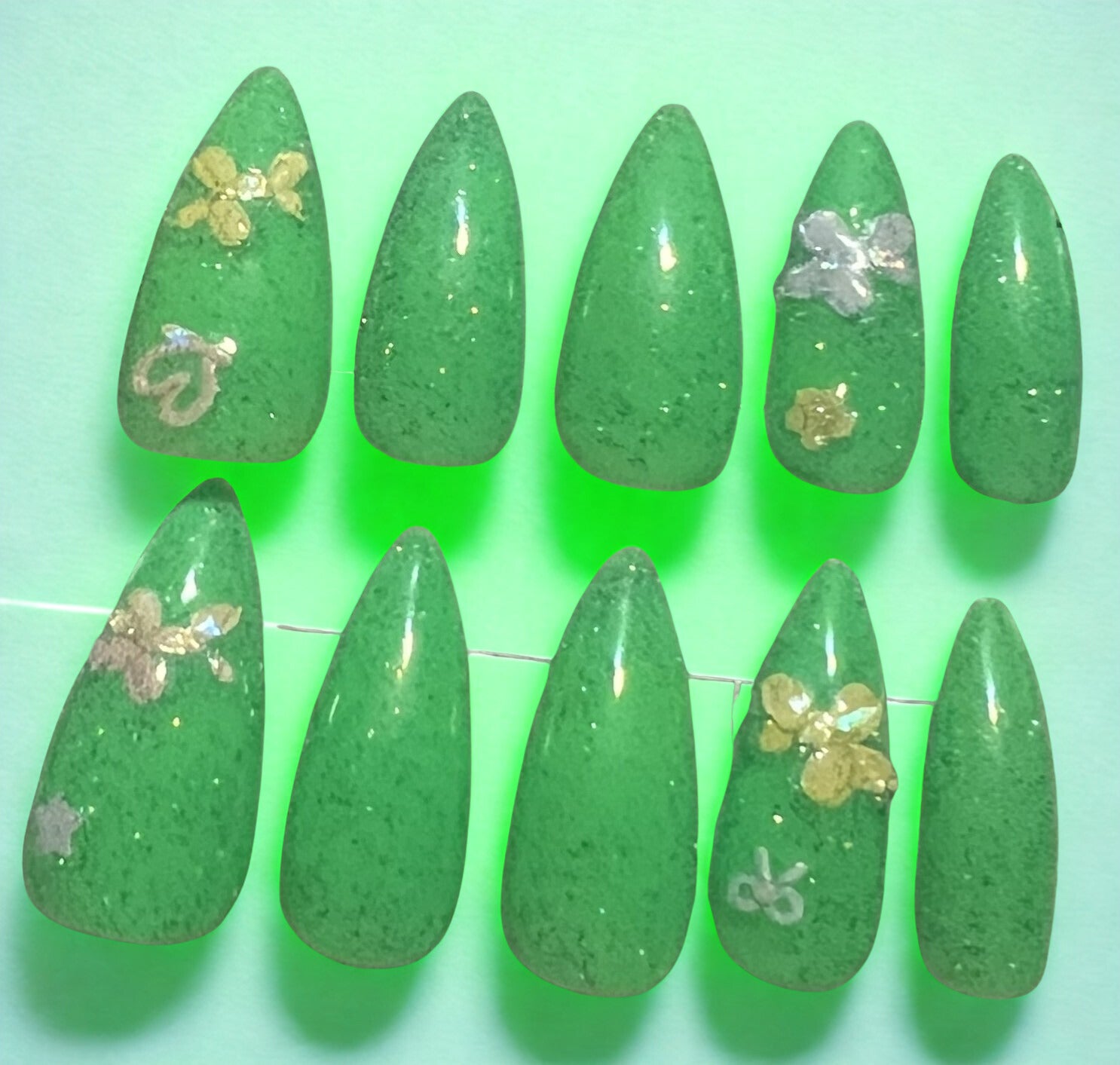 Legacy in Neon tribute press-on nails in neon green with a multi-colored holographic glitter topcoat. Decorated with stickers of balloon dogs, hearts, stars, and bows. Medium stiletto shape. Part of the Logan Harrel tribute collection available in pink, green, yellow, and orange.