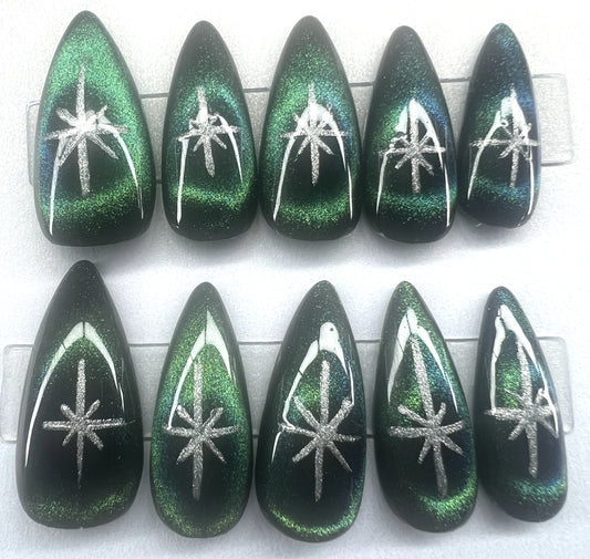 Hand painted stiletto press on nails featuring black base with green blue 9D cat eye circles and silver celestial stars.