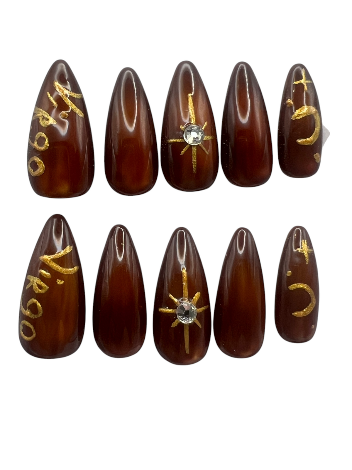 Medium length stiletto-shaped press-on nails featuring a deep chocolate brown jelly finish over a glowing glass cat-eye magnetic bead design. Hand-painted metallic gold art includes the word Virgo on the thumb, a celestial star with a centered clear rhinestone on the middle finger, and a crescent moon with small stars on the pinky finger.