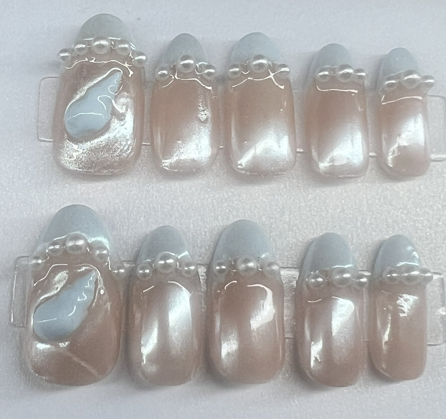 round bridal press on nails featuring a nude base, pale blue French tips, and a row of white pearls on each nail.