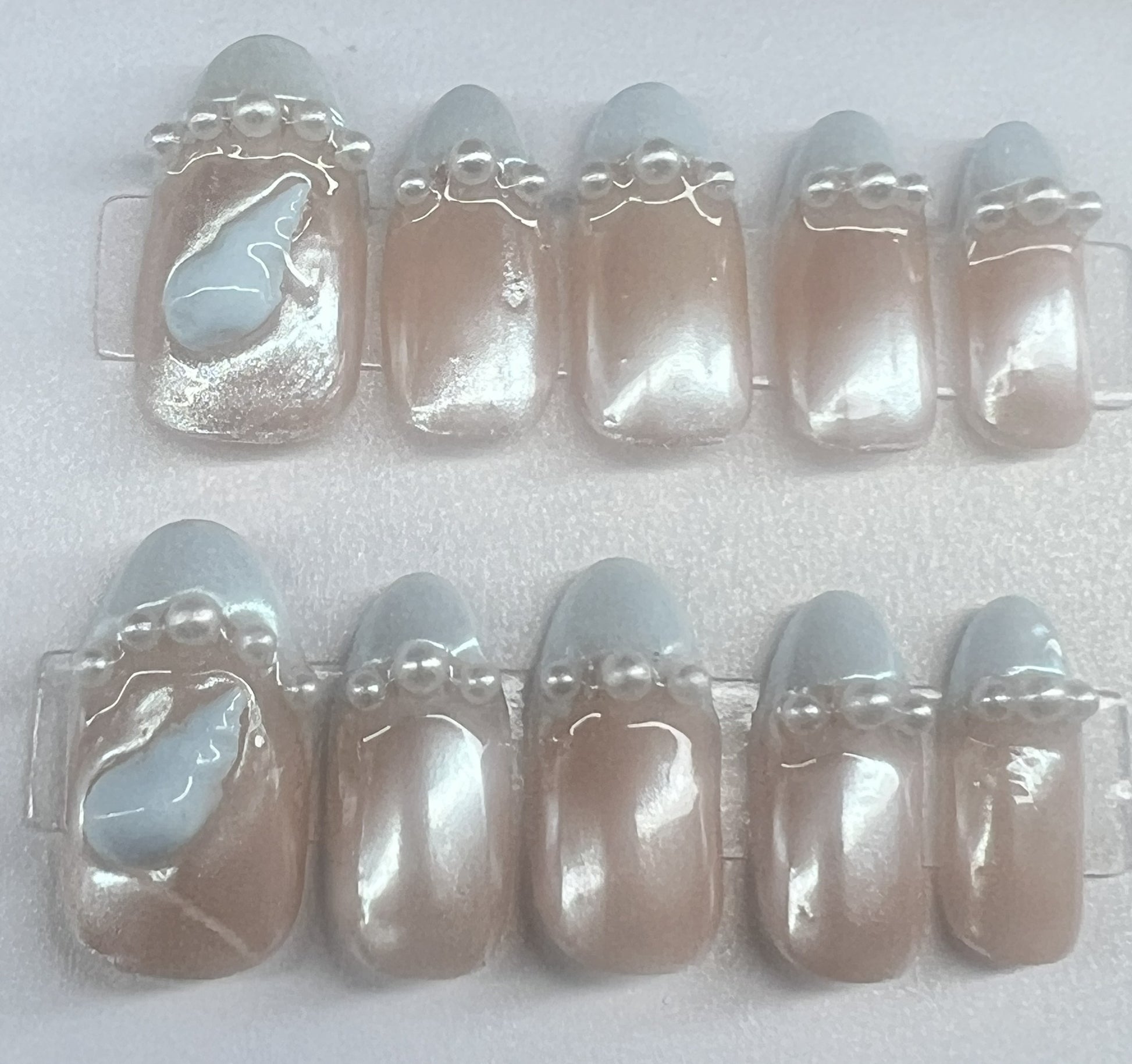 round bridal press on nails featuring a nude base, pale blue French tips, and a row of white pearls on each nail.