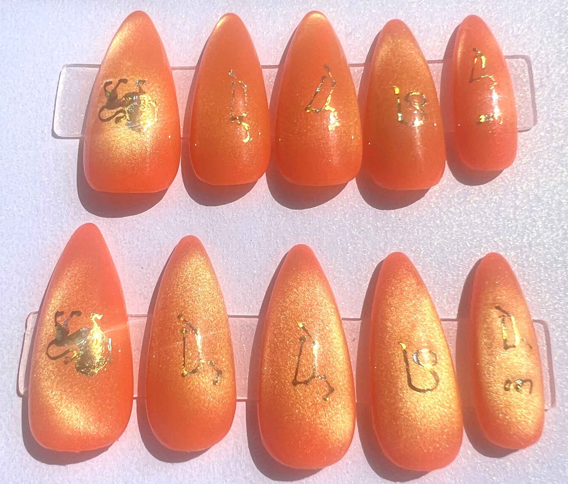 Medium stiletto-shaped press-on nails featuring a neon orange base color with a shimmering yellow jelly cat-eye magnetic effect. Each nail displays fine gold holographic Leo zodiac decals, including lion illustrations, stars, and astrology constellation symbols.