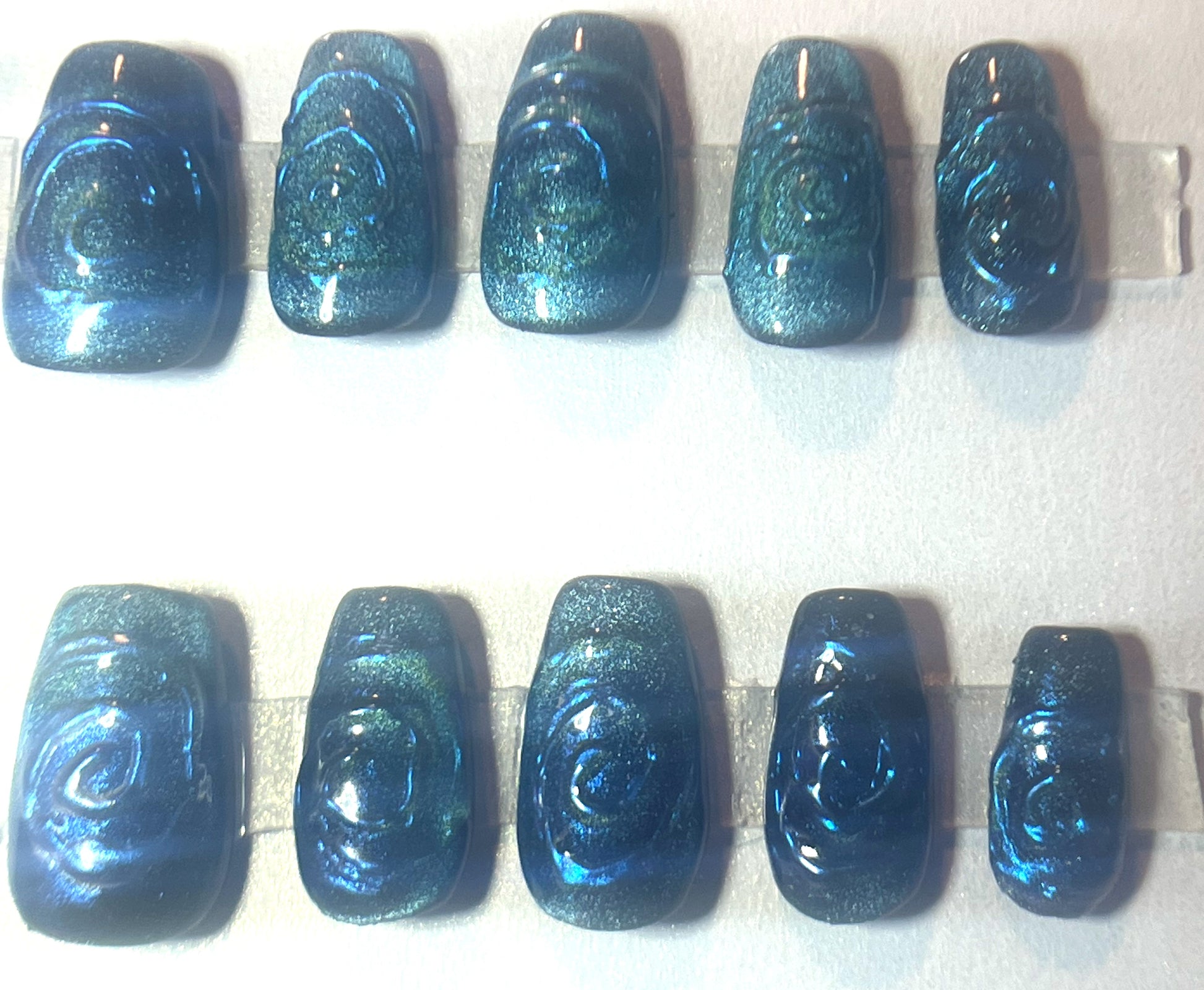 Luxury teal and blue velvet cat-eye press-on nails with 3D embossed swirl designs. The deep green-teal shimmer shifts to a rich cobalt blue under direct light. Ten custom short coffin nails with tactile spiral art.