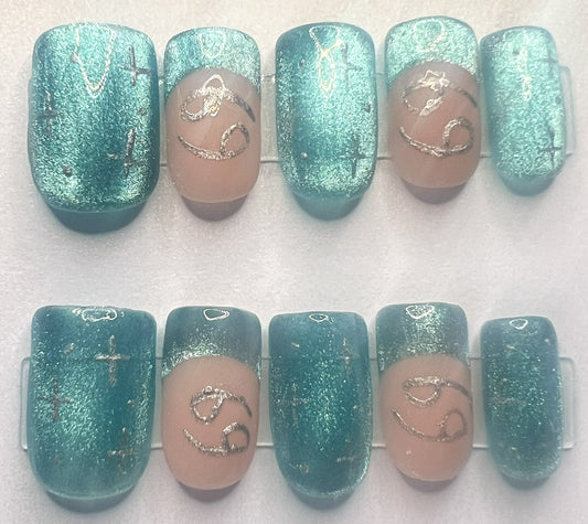 Short square press-on nails with a mismatched design. Three nails feature full-coverage deep teal green cat-eye gel polish with a shimmering wide velvet magnetic effect and tiny hand-painted silver 4-point stars. The remaining two nails feature classic nude French tips with teal velvet smiles and hand-painted silver Cancer zodiac symbols.